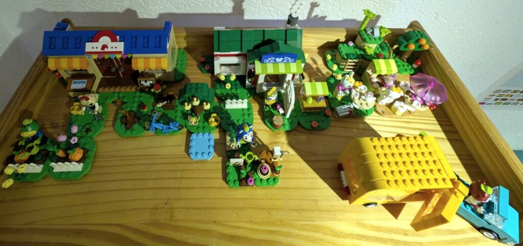 Blick von oben auf alle Legosets im Geschäftsviertel. Oben die beiden Geschäfte, davor Gärten, rechts der Wohnwagen, dahinter ein wenig Grün mit Bambus.