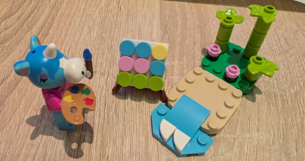 Das Set, bestehend aus Jimmy mit Palette und Pinsel vor der Leinwand, daneben ein Feld Strand mit Wasser und einer Rasenkachel mit Bambus.