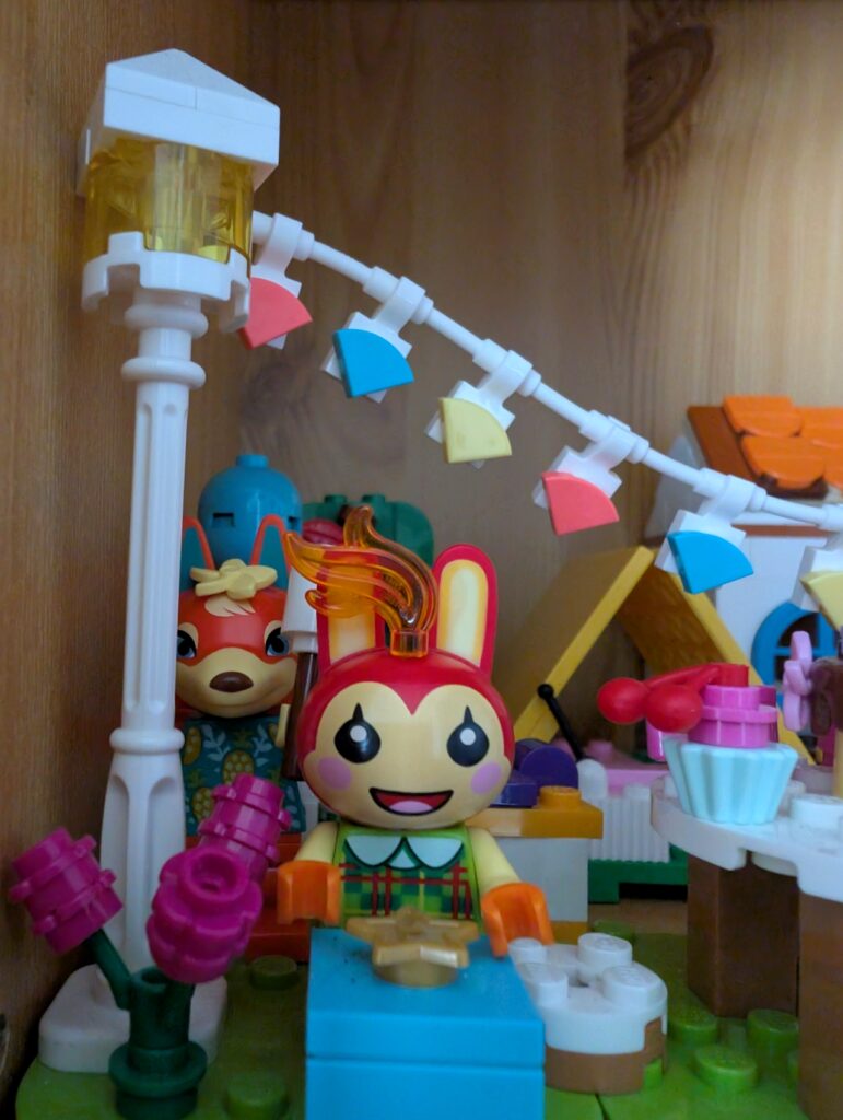 Nahaufnahme von Mimmi mit Feuer auf dem Kopf, dahinter Katharina mit nach oben gehaltenem Marshmallow am Stock.