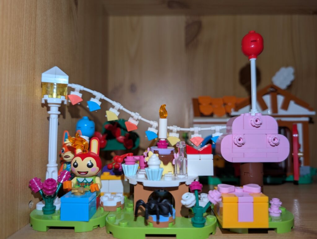 Blick auf das Partyset. Mimmi hinter einem Geschenk und dahinter Katharina. Auf einem Stuhl sitzt eine Spinne.