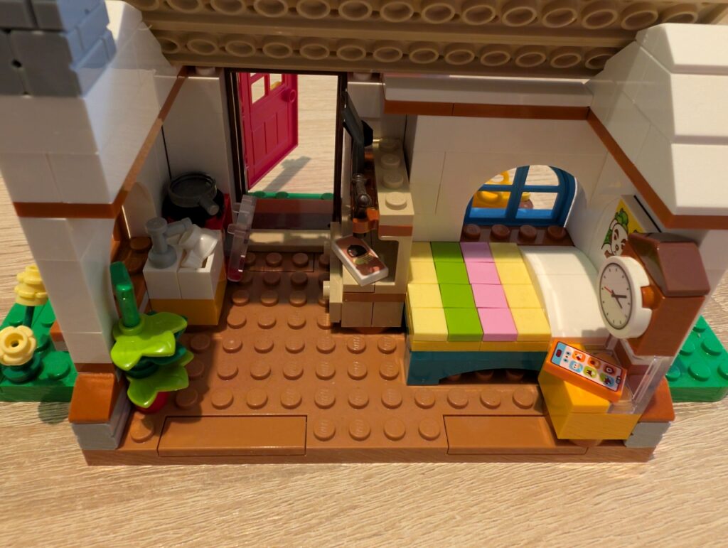 Braunes Haus, ebenfalls mit Bett, Tasse in der Spüle, gegenüber davon eine Werkbank. 
