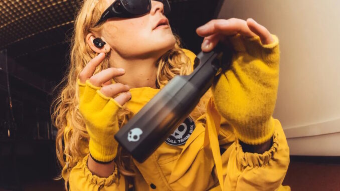 titelbild_method-360-anc Foto einer weiblichen Person in gelben Ganzkörperanzug mit Sonnenbrille. Sie hält das Case der Method 360 ANC in den Fokus der Kamera und hölt den Kopf schief, um ein In-Ear zu sehen.