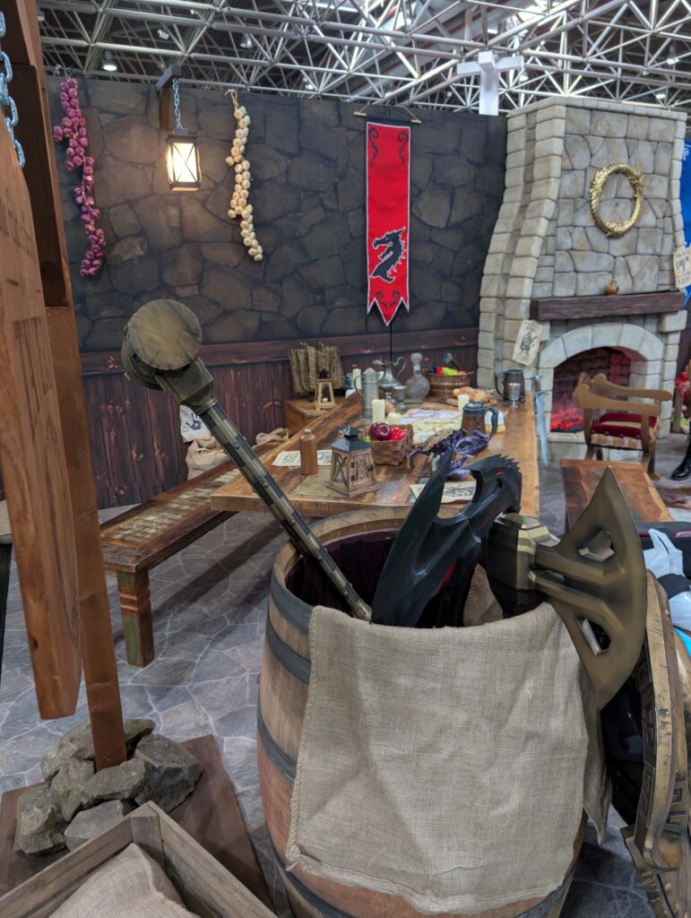 The Elder Scrolls Online-Kamin, davor ein Tisch mit falschem Essen, davor ein Fass mit falschen Waffen.