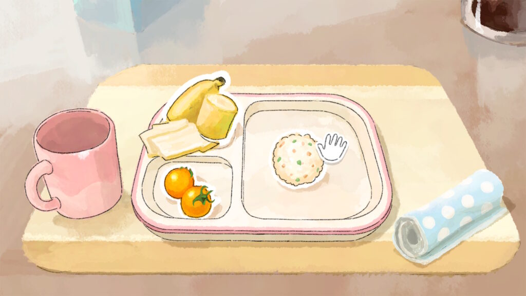 Kinderteller mit Unterteilung für verschiedene Komponenten einer Mahlzeit auf einem Brettchen. Auf dem Teller sind eine kleingeschnittene Banane, zwei Tomaten und ein Reisbällchen mit Gemüse. Daneben steht eine leere Tasse.