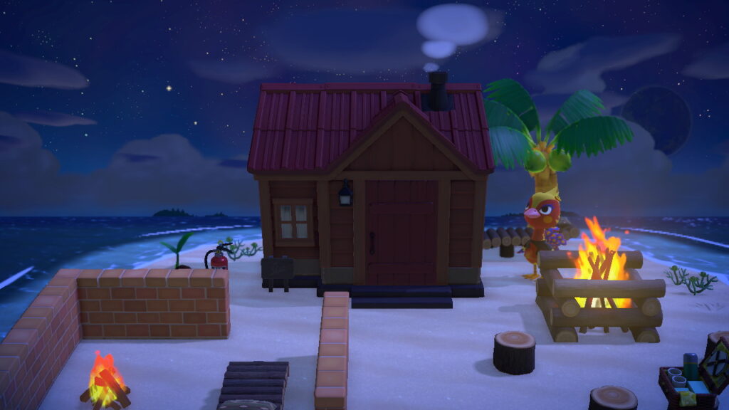 Frontaler Blick auf das Haus. Links niedrige Steinmauern, dahinter ein Feuerlöscher, rechts das große Feuer