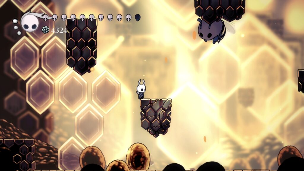 Screenshot aus einem Gebiet in Hollow Knight mit Bienen und von hinten beleuchteten Bienenwaben